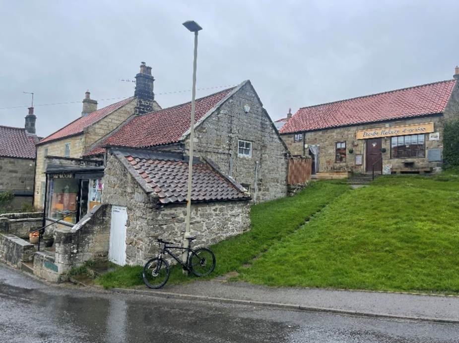 A stone building with a green lawn and a bicycle parked on the side of it

Description automatically generated
